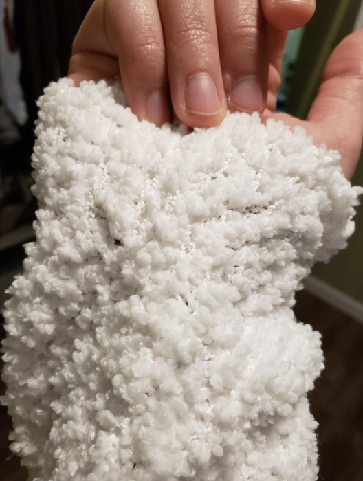 A close-up shot of a reviewer showcasing the sleeve detail of a white sweater.