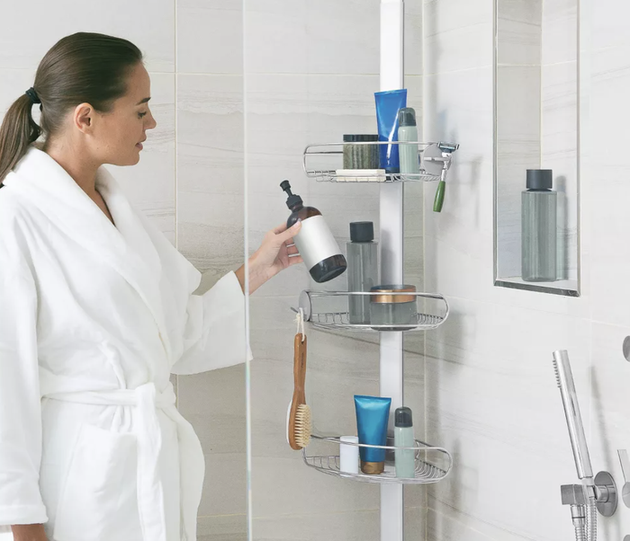 A model picking up a soap bottle from the corner of a sleek silver shower caddy.