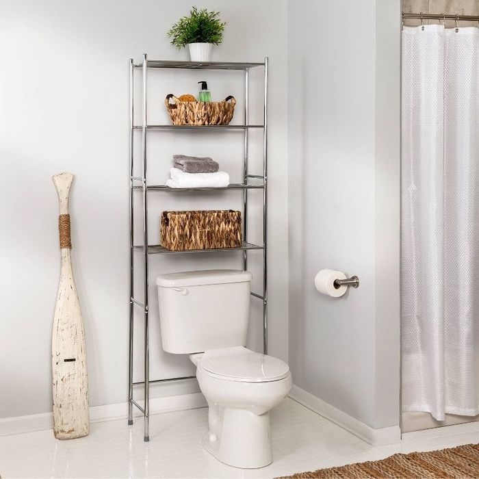 four-tier chrome storage unit placed above the toilet, with baskets, towels, and a plant decorating the shelves