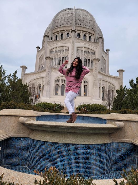 A reviewer strikes a pose atop a fountain, wearing a pink long-sleeve top adorned with black stripes.