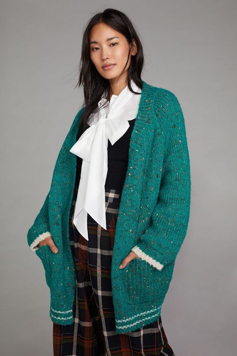 A model styling the green sweater over a black-and-white top paired with plaid pants for a chic, layered look.