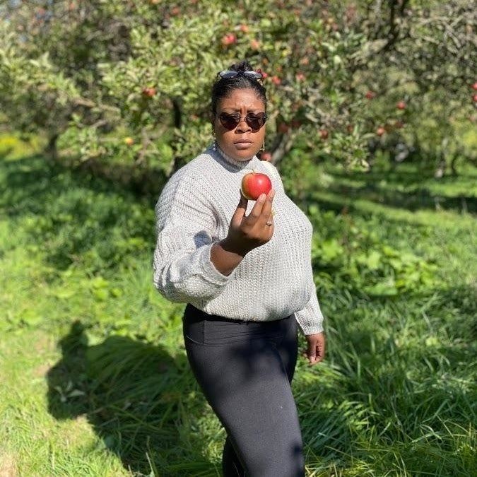 A reviewer's photo of a full-body outfit in an apple orchard, wearing the gray sweater