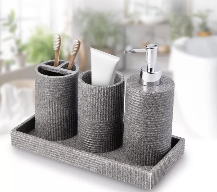 This gray four-piece bathroom accessory set includes a tray, toothbrush holder, pump dispenser, and cotton ball holder.