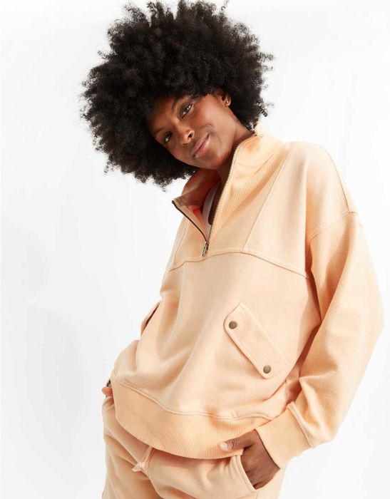 a model in a peach-colored half-zip sweatshirt