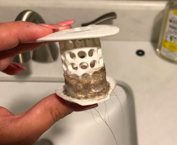 A reviewer holding the TubShroom after removing it from the drain, with hair visibly collected on it