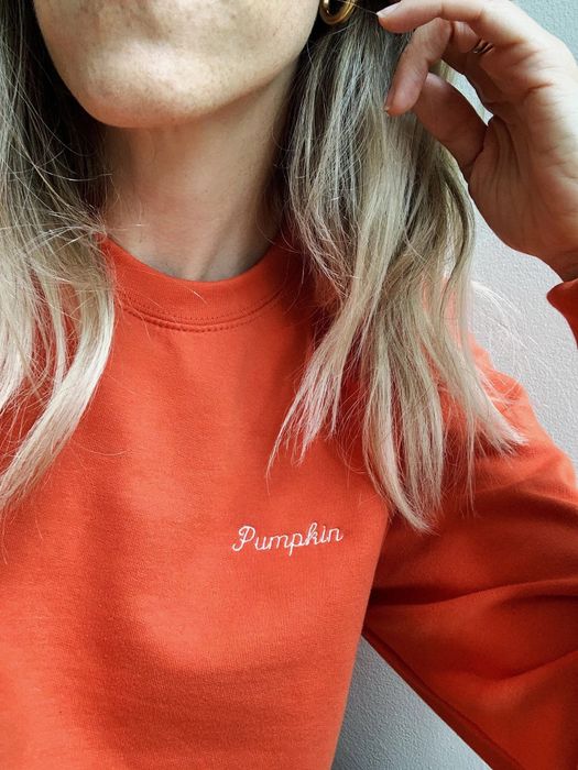 A detailed shot of a model showcasing the vibrant orange sweatshirt adorned with embroidered pumpkin designs.