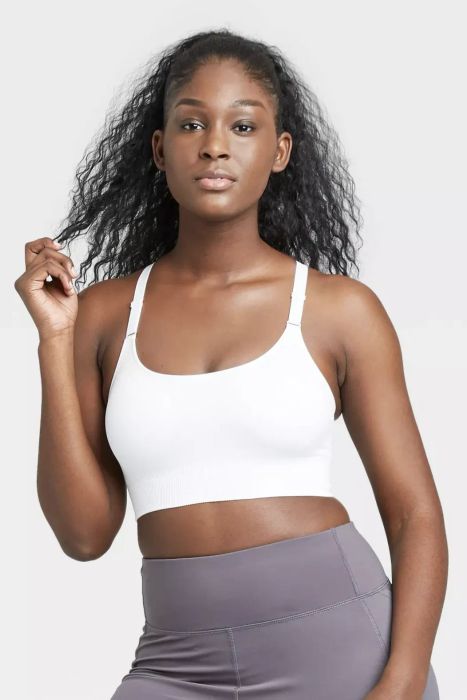 A model wearing a white sports bra paired with purple leggings against a white background.
