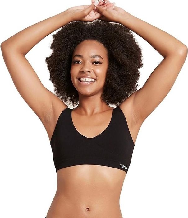 A cheerful woman in a black sports bra, raising her arms. Image utilized in a shopping article. No names provided