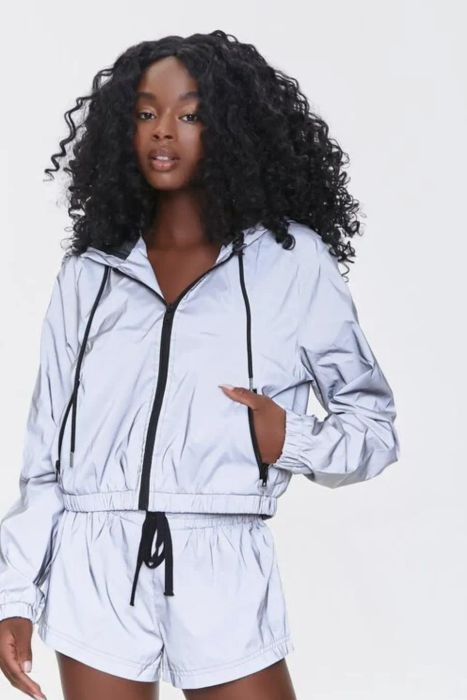 A model dressed in a matching silver reflective athletic jacket and shorts