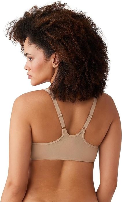 A curly-haired woman is photographed from behind wearing a beige bra