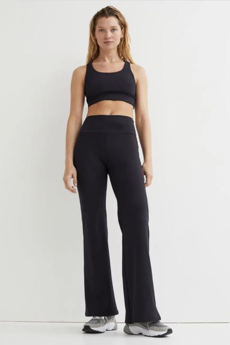 A model in black flared athletic pants paired with a sports bra and sneakers.