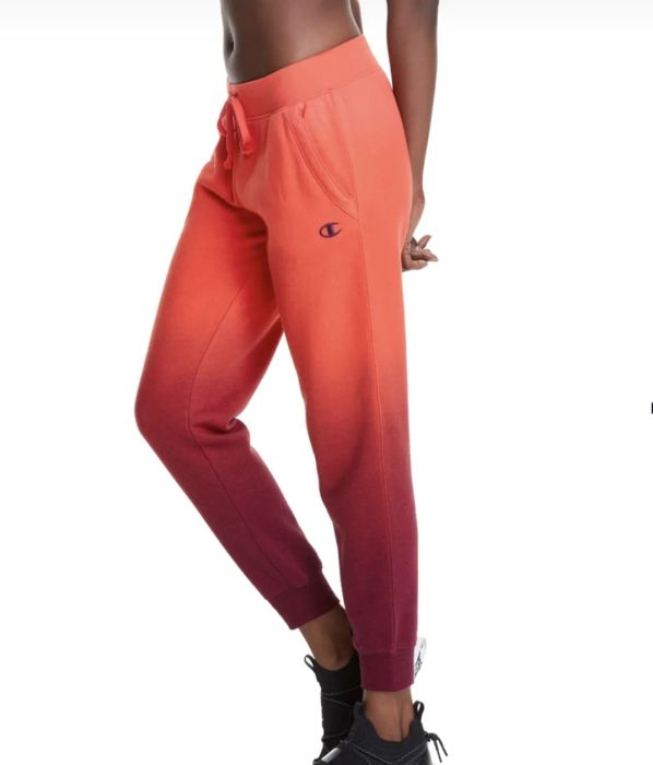 A model styled in orange and red dip-dyed fleece joggers paired with black sneakers, set against a white background