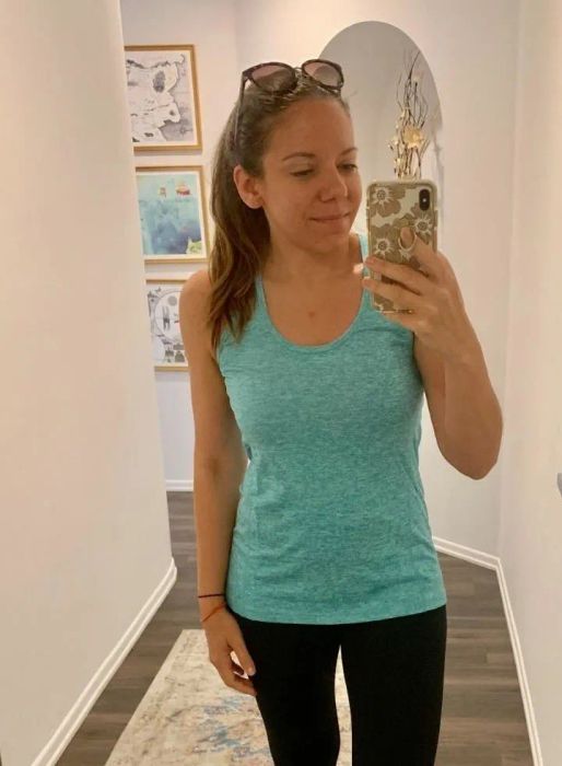 A reviewer models a teal sports tank top with sunglasses perched on their head.