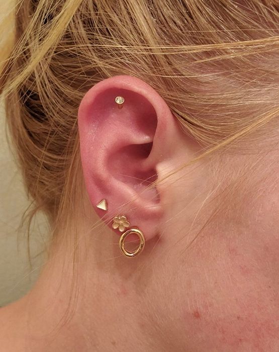 A person showing off three studs in their multiple ear piercings.