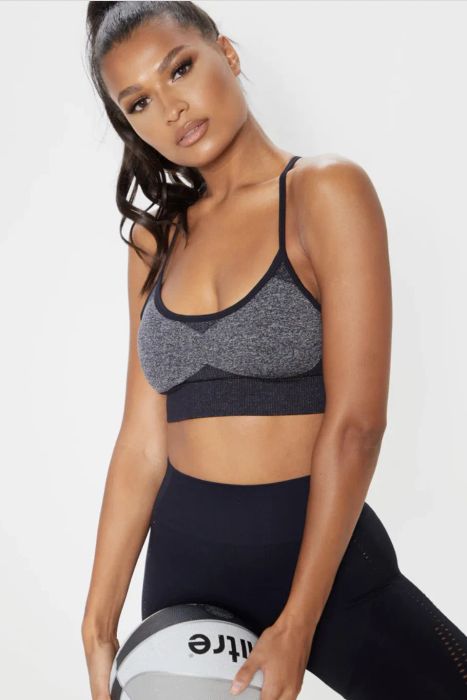 A model dressed in black leggings and a black-and-gray crop top, holding a ball.