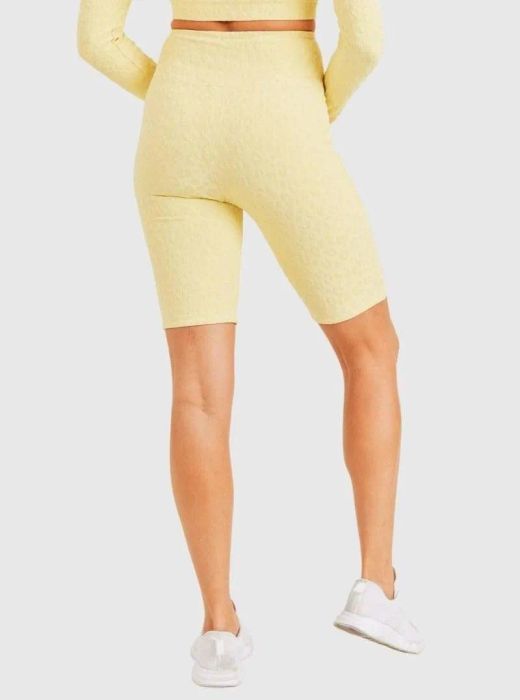 A model is styled in yellow leopard-print biker shorts, paired with white running sneakers for a bold and sporty look.