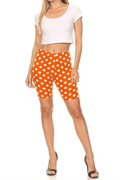 A model showcasing orange shorts with white polka dots, paired with a white top and heels