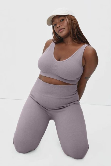 A model in a purple sports bra paired with matching leggings and a white baseball hat.