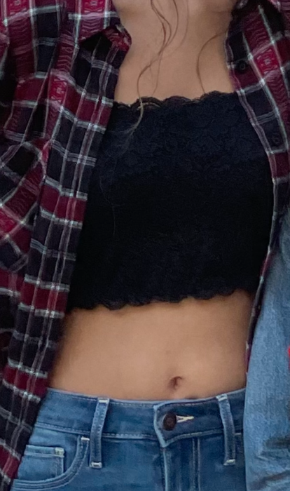 A woman styled in a black lace crop top paired with a red plaid shirt and blue jeans