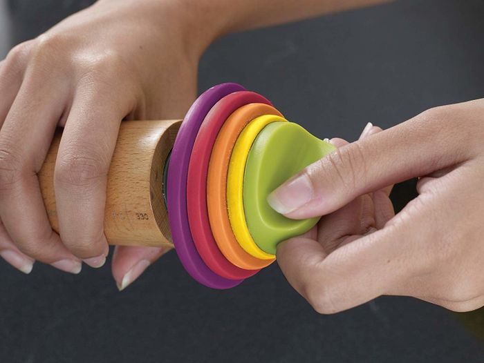 a model displaying the adjustable end of the rolling pin with five different size options in various colors