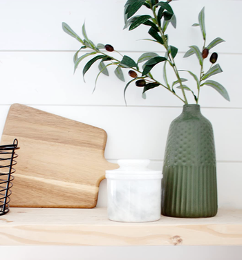 A wooden cutting board, a white ceramic jar, and a textured green vase holding a plant, creating a lovely kitchen vignette.