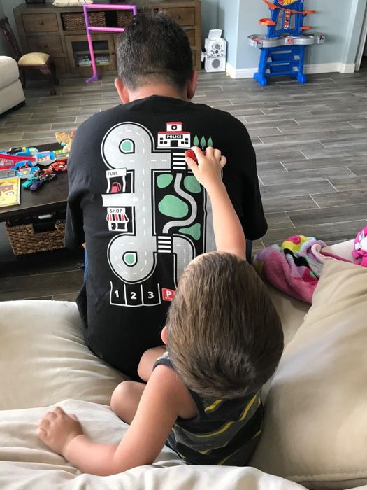 A child plays with a car on a racetrack design printed on the back of a shirt worn by a person