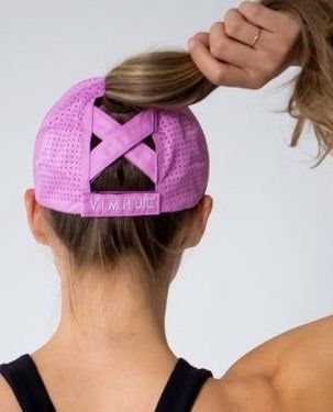back view of a model wearing the purple cap with a high ponytail, showcasing the X design on the back of the cap