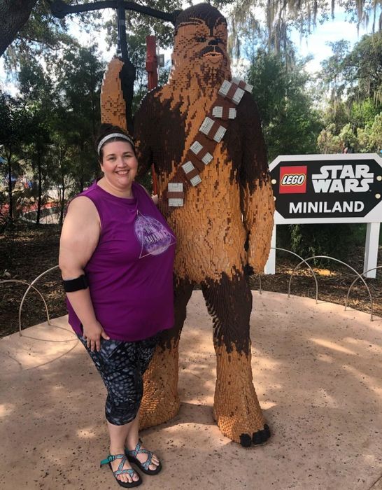 A reviewer stands next to a giant Chewbacca statue while wearing gray butterfly leggings.
