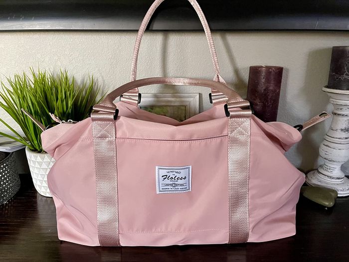 A soft pastel pink duffel bag featuring a distinctive white logo tag