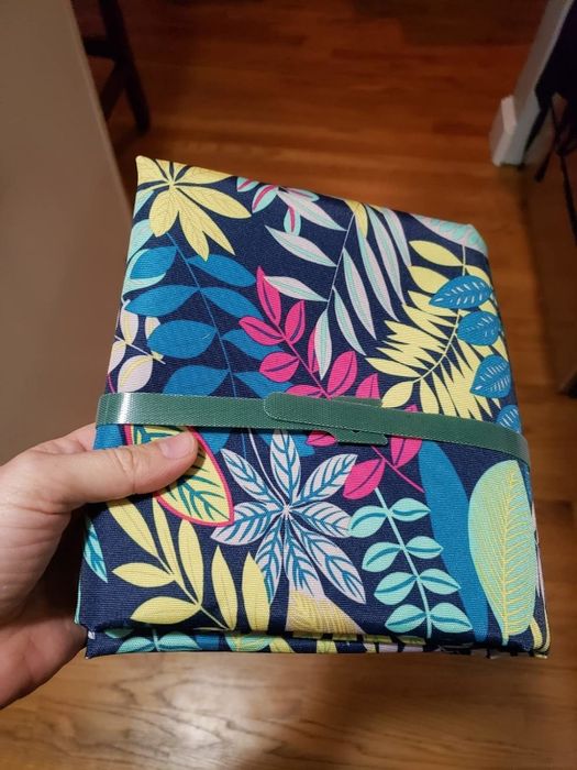 A person showcasing a fabric wallet with a floral pattern, secured by a green elastic band.