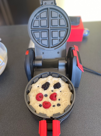 A waffle maker filled with uncooked batter and topped with fresh berries.