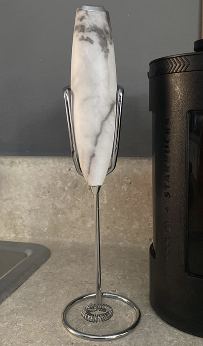 A reviewer’s photo of a sleek white marble handheld frother resting on its stand