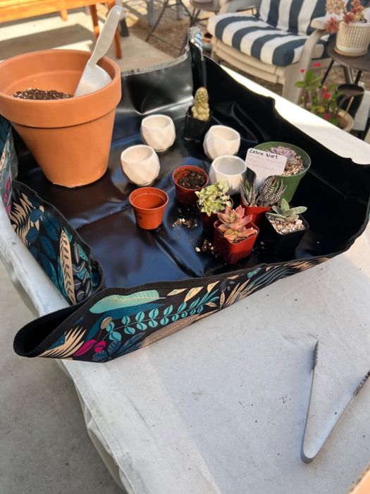 A gardening apron with handy pockets for storing tools and plants, displayed on an outdoor table alongside various garden items.