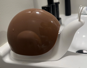 A brown, snail-shaped soap dispenser placed on a bathroom sink