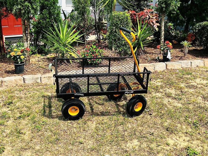A black wagon with a yellow handle, sitting on the grass, ready for use.