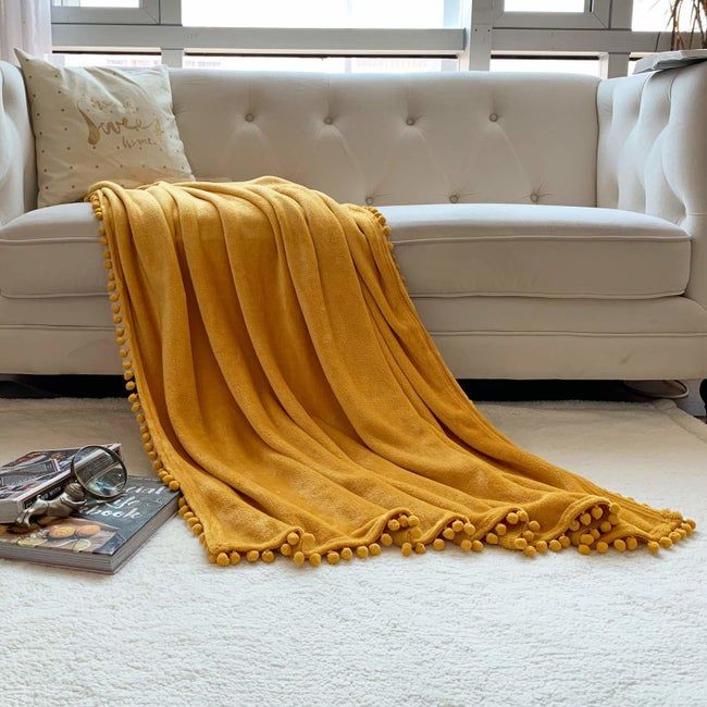 A cozy mustard yellow blanket featuring pom-pom trim, draped elegantly over a couch