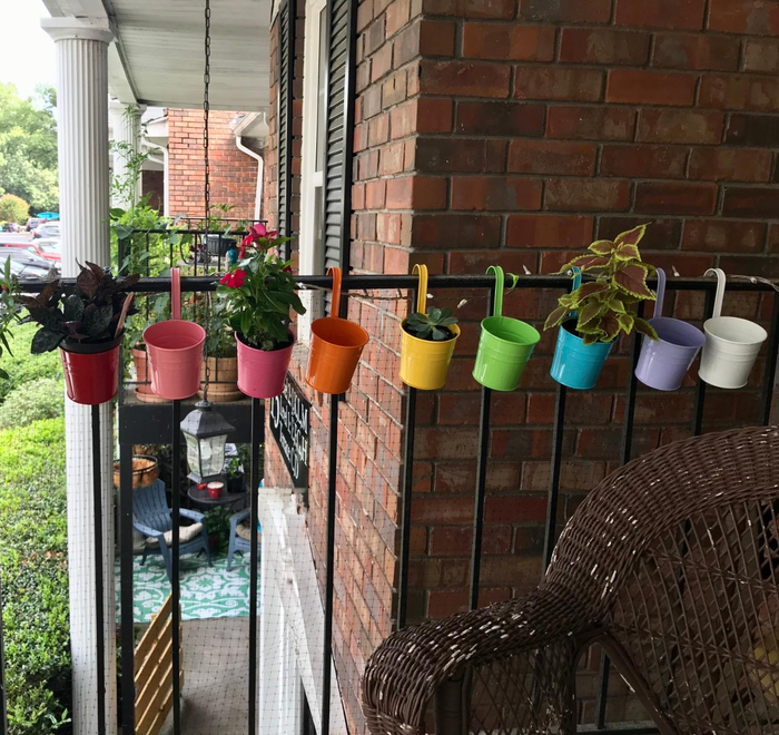 A variety of colorful planters arranged along a balcony railing, providing creative apartment gardening ideas.