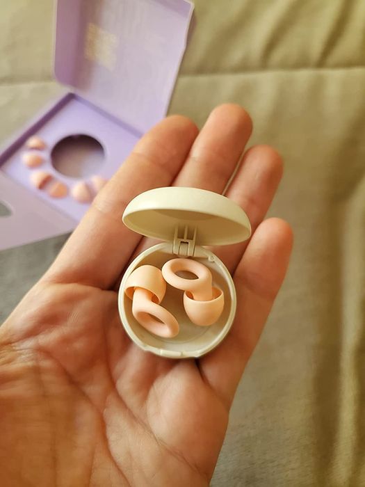 A pair of pink earplugs held in a reviewer's hand, showcasing their sleek design.