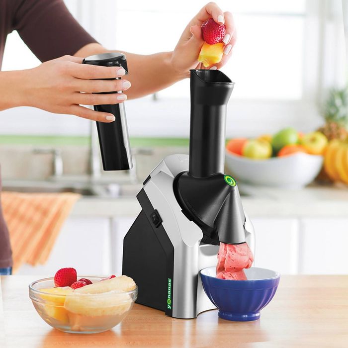 A person loading frozen fruits into the Yonanas machine, which is producing a smooth soft-serve dessert.