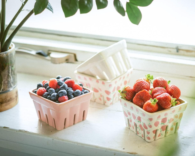A collection of fresh, assorted berries arranged in decorative baskets placed on a windowsill.