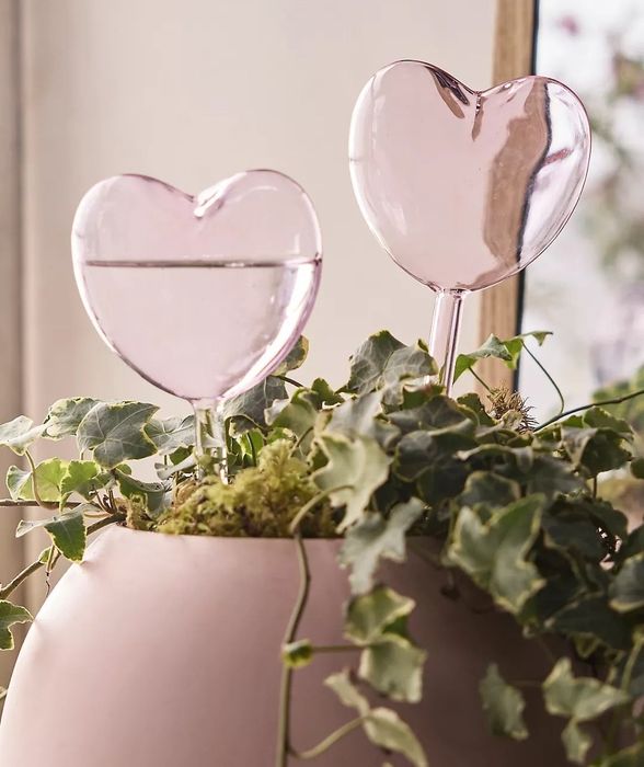 Two heart-shaped glasses in a pink vase with ivy, perfect for a romantic table setting.