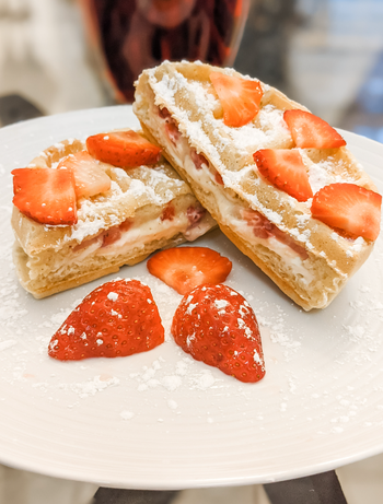 A plate of strawberry cream puff pastry, lightly dusted with powdered sugar, accompanied by freshly sliced strawberries.