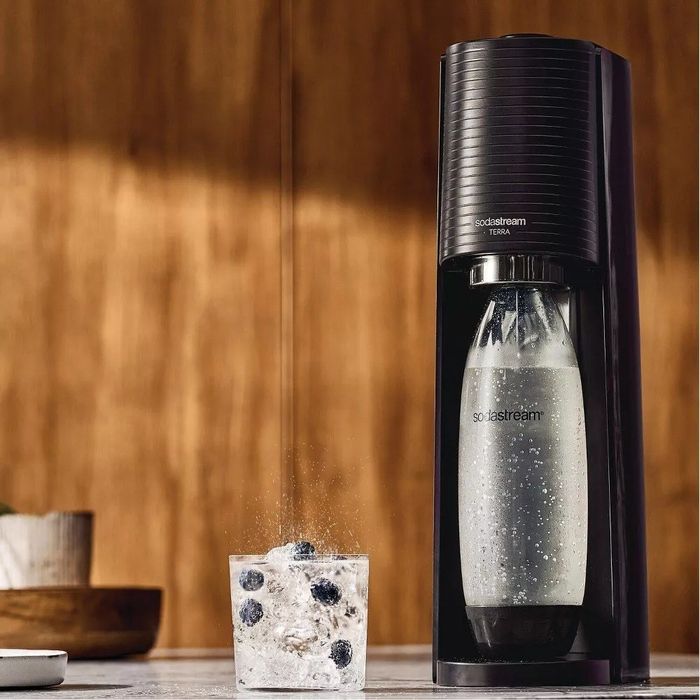 A SodaStream next to a glass of sparkling water filled with berries.