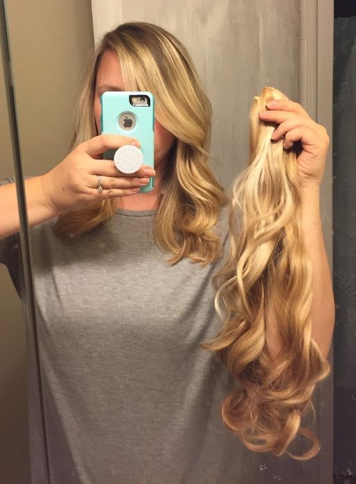 A reviewer holding a pair of blonde hair extensions.