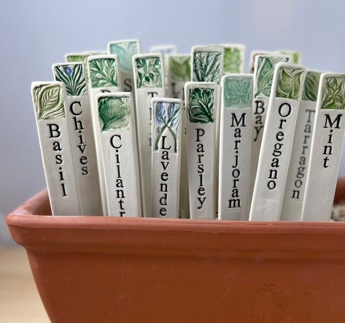 Ceramic herb markers placed in a terracotta pot, labeling different types of herbs for a garden setup