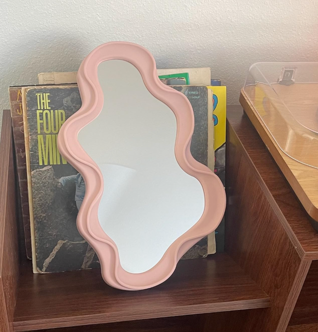A wavy-edged mirror perched on a wooden shelf with books neatly arranged in the background.