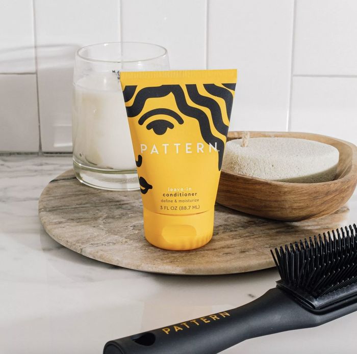 A tube of leave-in conditioner, a hair brush, and a candle