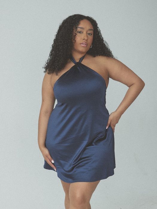 A model wearing a halter neck dress, striking a pose with one hand on her hip.
