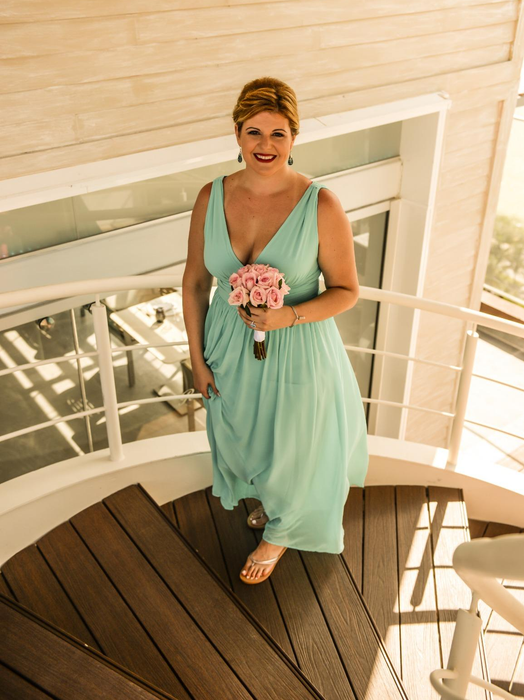 A reviewer is pictured in a flowing, sleeveless v-neck gown, holding a bouquet while standing on a staircase.