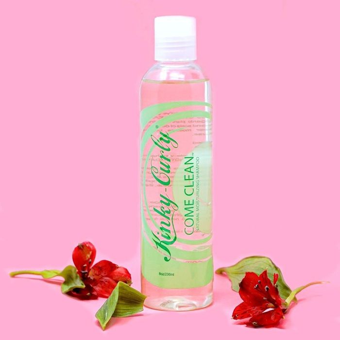 A bottle of the Come Clean shampoo pictured alongside vibrant red flowers.